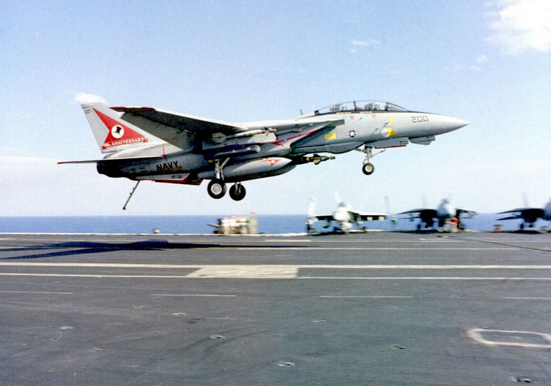 F-14 “Томкэт” из 14-й истребительной эскадрильи ВМС США совершает посадку на палубу авианосца “Теодор Рузвельт” после боевого вылета на Балканах 5 мая 1999 года. Самолет несет нестандартную парадную окраску в честь 80-тилетия эскадрильи. [U.S. Navy]